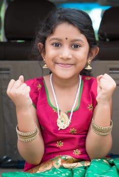 Excited Indian girl sitting in car smiling, ready to vacation. Asian child in traditional dress.
