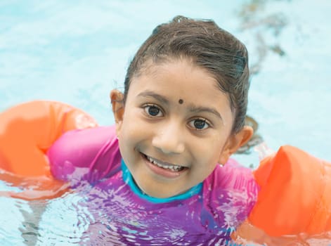Indian child learning swimming in pool. Asian kid in swimmer class with float bands.