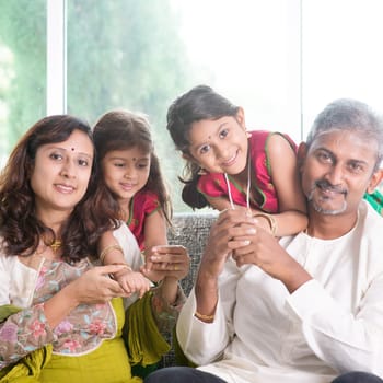 Happy Indian family at home. Asian parents with their kids, sitting on sofa. Parents and children indoor lifestyle.
