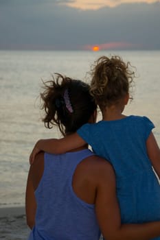 Mother and daughter sitting on the beach at sunset
