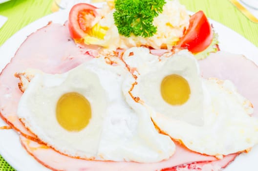 Two fried eggs in heart shape in the pan. The overall picture looks like a face made of fried eggs.