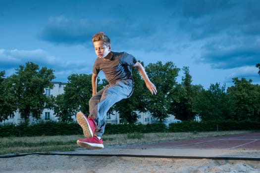 Side frontal full body view of a male young teenager frozen while jumping into a long jump pit