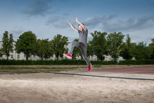 Side frontal full body view of a male young teenager frozen while jumping into a long jump pit