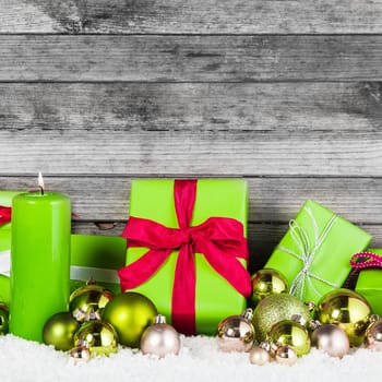 Close up Green and Silver Christmas Items like Candles, Presents and Balls, on Snow with Rustic Wall Background.