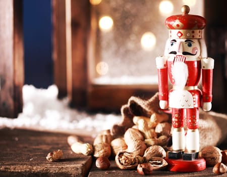 Close up Nutcracker Toy and Nuts on Wooden Table Near Window Pane. Captured on Christmas Holiday Season.