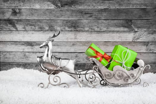 Close up Attractive Christmas Ornaments - Metallic Reindeer and Sleigh with Green Christmas Gifts on the Snow with Rustic Wall Background.