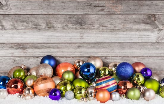 Close up Assorted Colored Christmas Balls Decorations on Snow with Vintage Wooden Wall Background.
