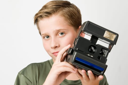 Frontal torso view of a 13-year-old teenager against a white background holding an instant camera in front of him and looking friendly into the camera
