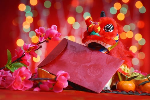 Chinese new year festival decorations, miniature dancing lion and ang pow or red packet with copy space ready for text, on glitter red background.