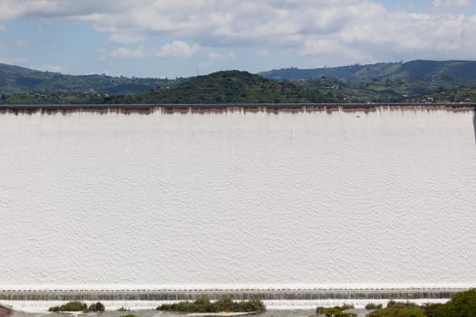 Dam wall full flowing river water over weir wall into summer valley.