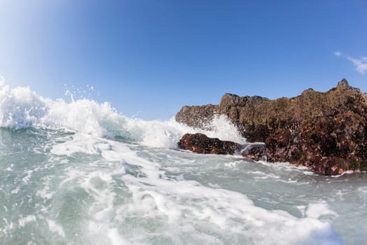 Ocean waves shore break crashing into rocks along beach coastline swimming closeup detail.