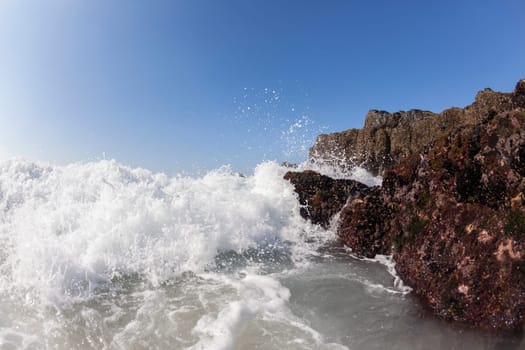 Ocean waves shore break crashing into rocks along beach coastline swimming closeup detail.