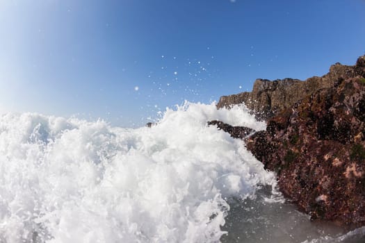 Ocean waves shore break crashing into rocks along beach coastline swimming closeup detail.