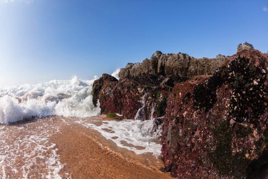 Ocean waves shore break crashing into rocks along beach coastline swimming closeup detail.