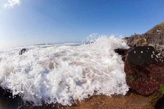 Ocean waves shore break crashing into rocks along beach coastline swimming closeup detail.