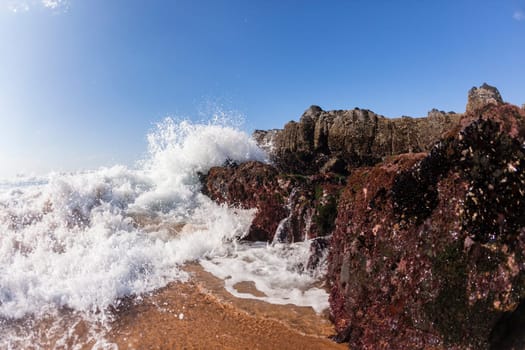Ocean waves shore break crashing into rocks along beach coastline swimming closeup detail.