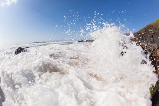 Ocean waves shore break crashing into rocks along beach coastline swimming closeup detail.