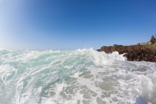 Ocean waves shore break crashing into rocks along beach coastline swimming closeup detail.
