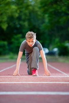deep front full body view of a young male teenager looking in depth starting position on a tartan track in the camera