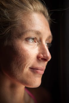 Side head portrait of a smiling middle-aged blonde woman in the side window light