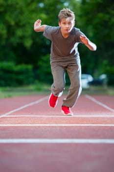 Frontal full-body view of a young male teenager on a tartan track towards the camera