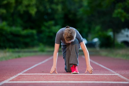 Deep frontal full-body view of a young male teen in low-start position on a tartan track looking into the camera