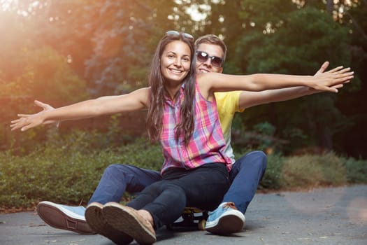 Young happy couple in love sitting on a skateboard outdoors