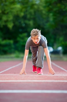 Deep frontal full-body view of a young male teen in low-start position on a tartan track looking into the camera