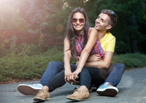 Young happy couple in love sitting on a skateboard outdoors