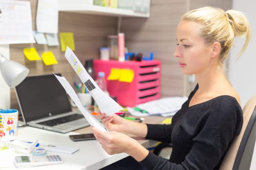 Business and entrepreneurship consept. Beautiful blonde business woman working in colorful modern creative working environment reviewing some papers.