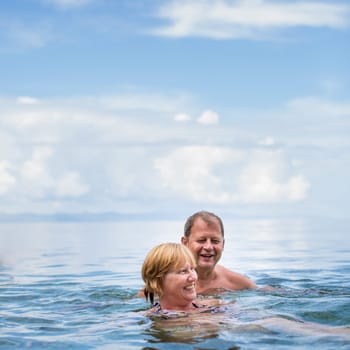 Senior couple enjoying the retirement on a seacost, having a swim in the sea, laughing togther, staying active and positive