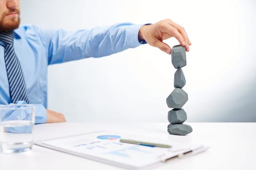 Modern businessman building tower from grey stones on workplace