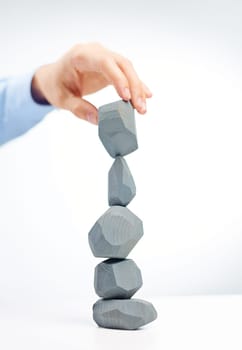 Human hand holding grey stone over stone tower