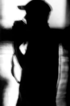 The black silhouette and shadow of a photographing man wearing a baseball cap on a white linen cloth.