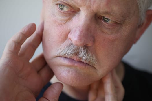 Senior man touches his sore jaw area.