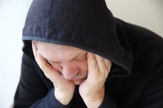 Senior man wearing a dark hoodie slumps in depression.