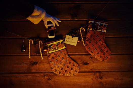 Christmas socks, sugar canes, toy bubbles on wooden background and cellphone bound with ribbon in gloved Santa hand