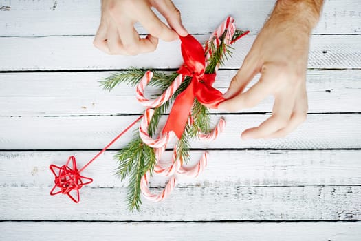 Human hands binding Christmas bouquet made up of candy canes, red star and conifer