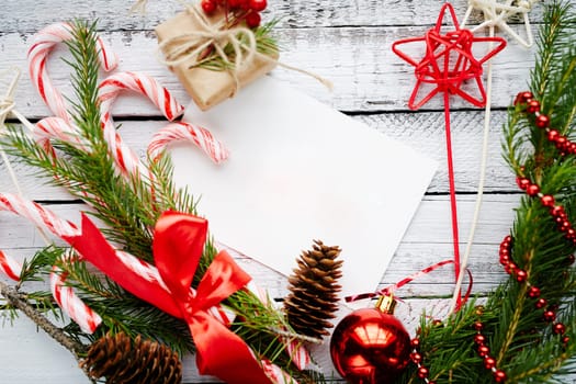 Christmas composition made up of conifer branches, cones, decorative bubble, stars, beads, candy canes and small giftbox on wooden background