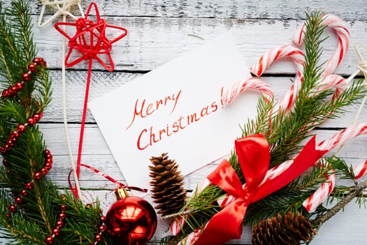 Christmas composition made up of conifer branches, cones, decorative bubble, stars, beads, candy canes and greeting card on wooden background