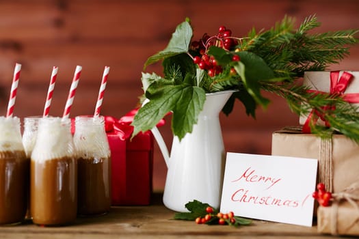 Vase with guelder leaves and berries, bottles with hot chocolate topped with whipped cream and several giftboxes
