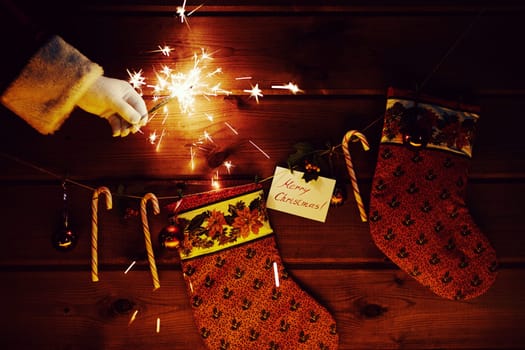 Christmas socks, candy canes, decorative bubbles and Bengal light in gloved Santa hand near by