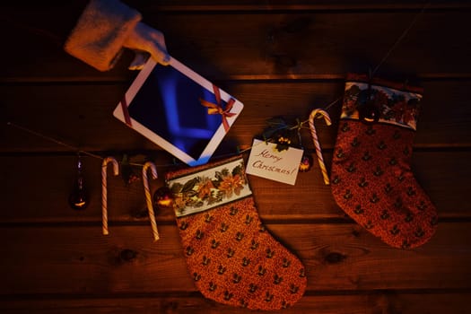 Christmas socks, sugar canes, toy bubbles on wooden background and touchpad bound with red ribbon held by Santa