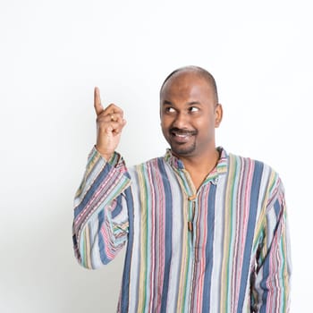 Indian casual man hand pointing up to something, copy space, standing on plain background.