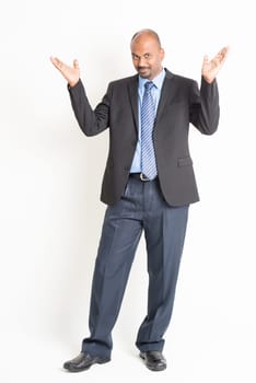 Portrait of full body mature Indian business man open arms as like showing something, standing on plain background.