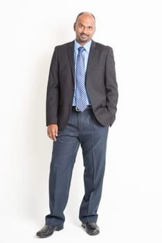 Portrait of full body mature Indian business man arms crossed, standing on plain background.