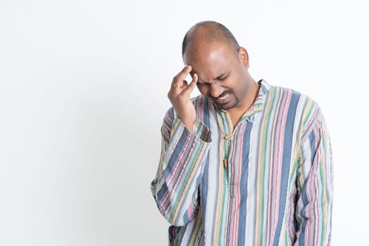 Portrait of Indian mature man having headache, hand rubbing forehead, standing on grey background.