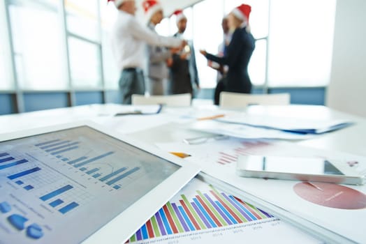 Documents and touchpad with data at workplace on background of toasting colleagues