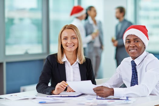 Two happy employees looking at camera on Christmas eve in office