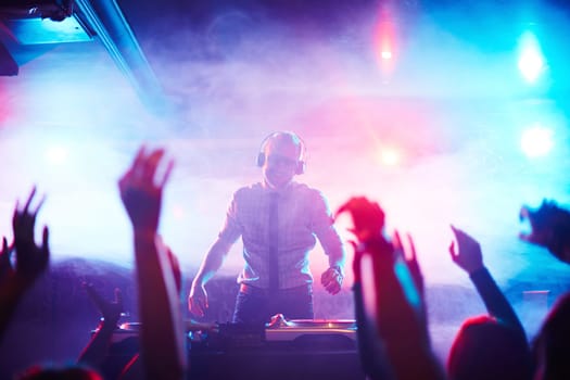 Male deejay standing by turntables in front of dancing crowd at disco